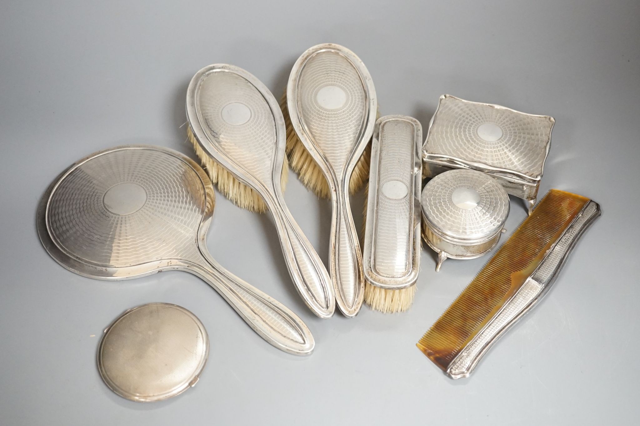 A George V engine turned silver seven piece dressing table set, comprising, two trinket boxes and a mirror, brush and comb set, Synyer & Beddoes, Birmingham, and Chester, 1912,13,14 and a silver mounted compact.